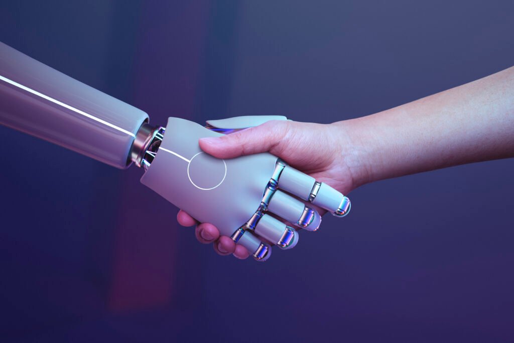 A person and a robot hand clasping in a handshake, illustrating the merging of technology and humanity (AI)